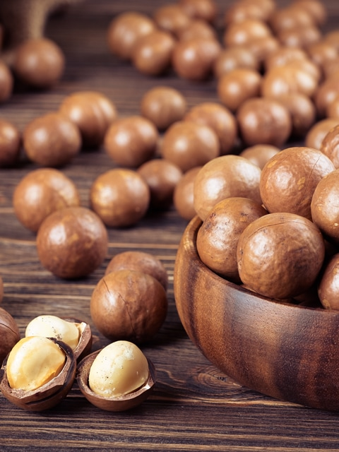 Macadamia nuts in a wooden bowl with cracked shells and kernels