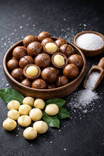 A bowl of macadamia nuts with whole kernels, green leaves and salt